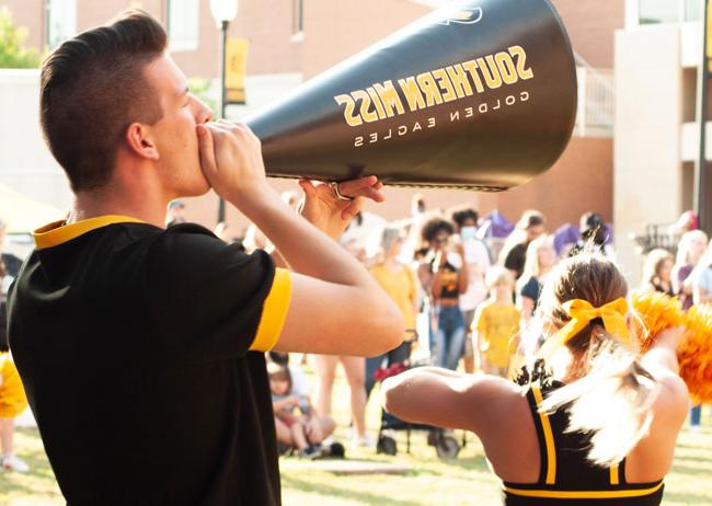 Southern Miss cheerleader shouting into megaphone at Friday night pep rally at Spirit Park